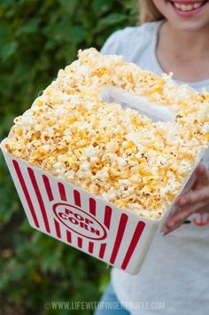 a woman is holding a box of popcorn