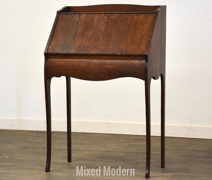 an old wooden desk sitting on top of a hard wood floor next to a white wall