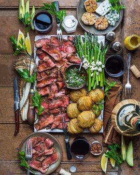 an assortment of meats, vegetables and sauces on a wooden table with utensils