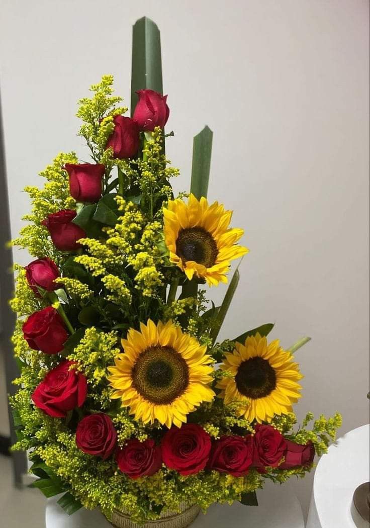 a vase filled with red roses and yellow sunflowers on top of a table