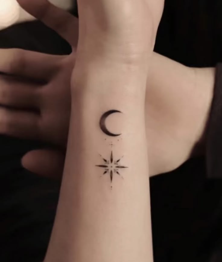 a woman's wrist with a small star and moon tattoo on her left arm