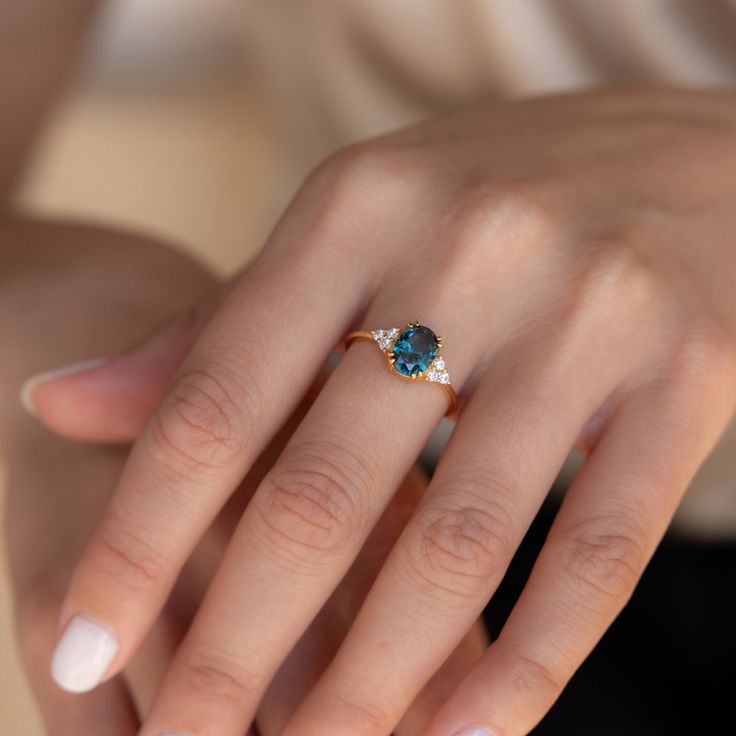 a woman's hand holding a ring with a blue topazte on it