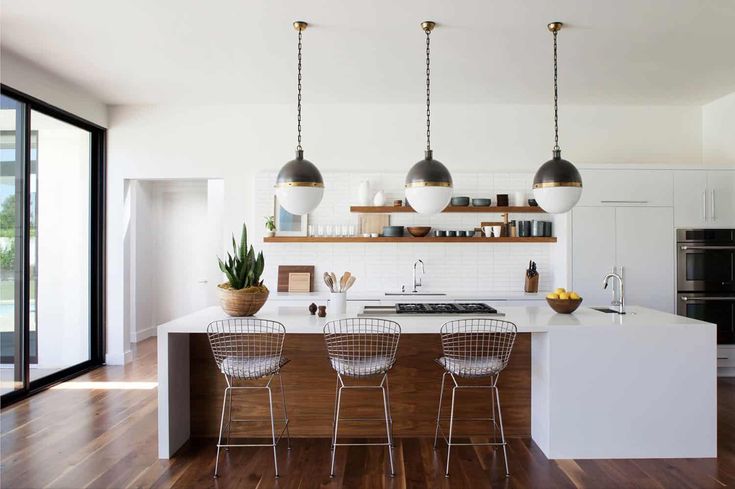 a kitchen with three hanging lights over the island and four chairs in front of it