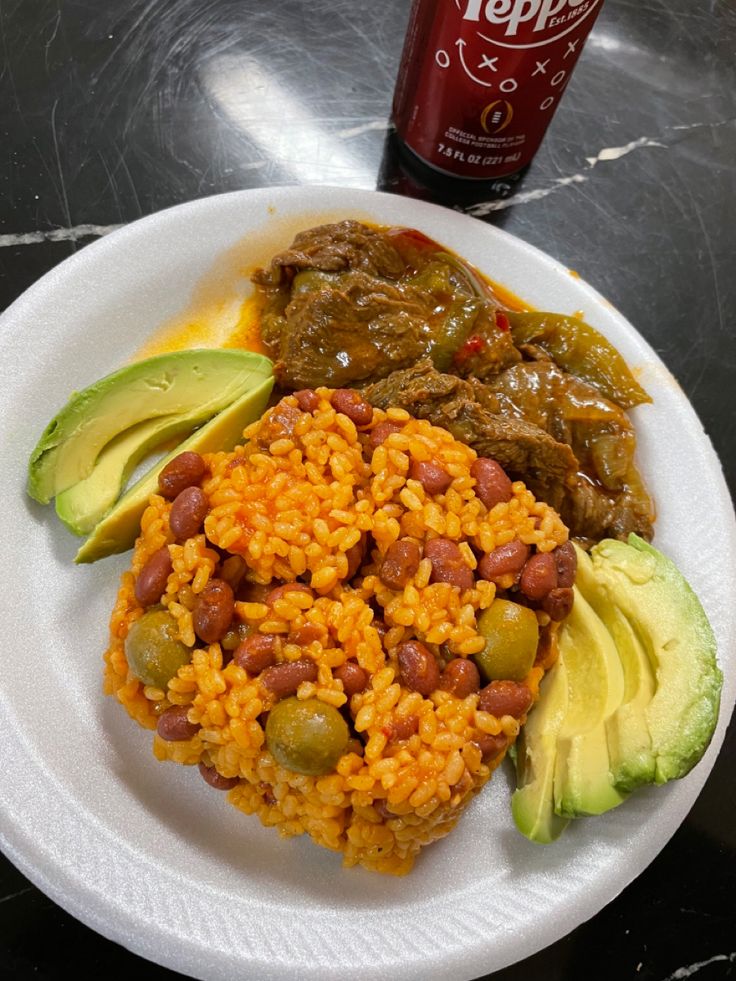 a white plate topped with rice, beans and avocado next to a soda