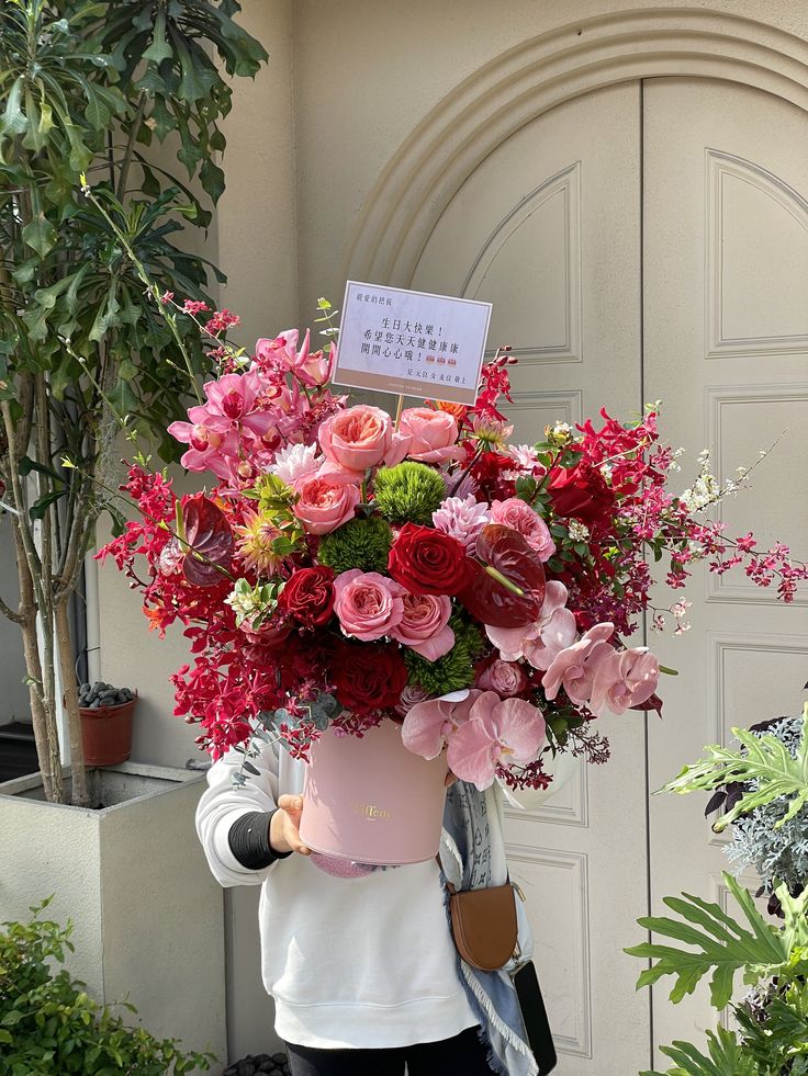 a woman holding a large pink vase filled with lots of flowers next to a door