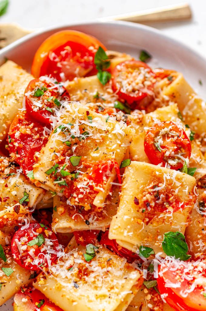 a white bowl filled with pasta and tomatoes covered in parmesan cheese on top