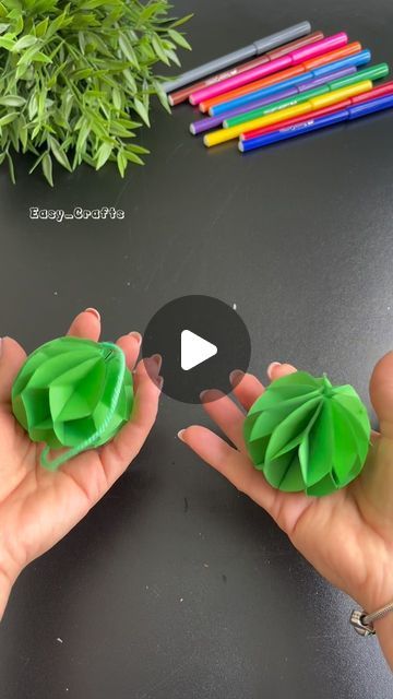 two hands holding green origami flowers with colored crayons in the background