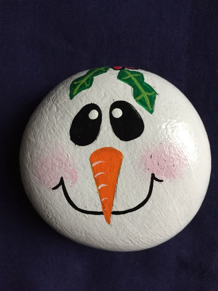 a painted rock with a smiling face and carrot on it's nose, against a blue background