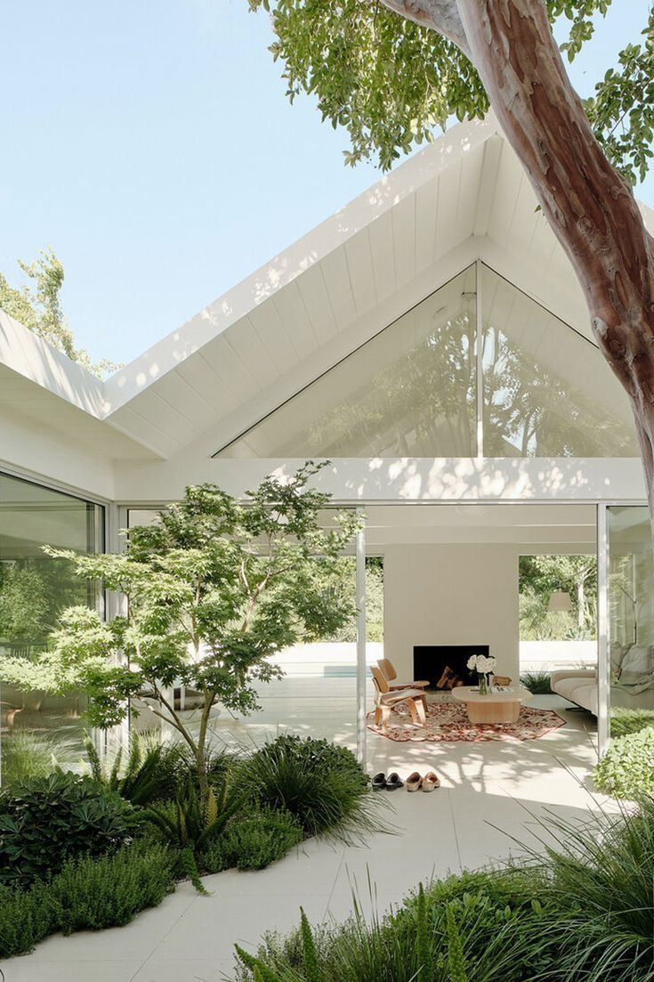 the interior of a house with white walls and ceilings is filled with green plants, trees, and an open fire place