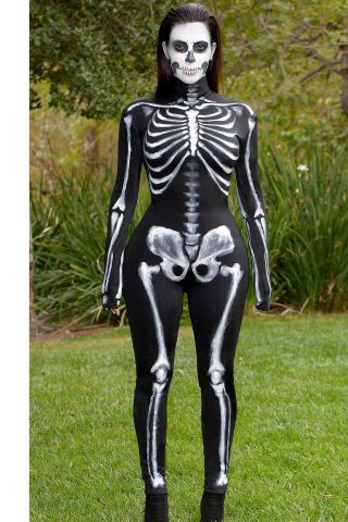 a woman in skeleton costume standing on the grass with her hands behind her back to the camera