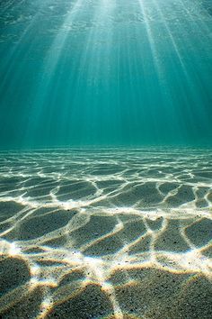 the sun shines brightly through the water's surface as it floats over sand