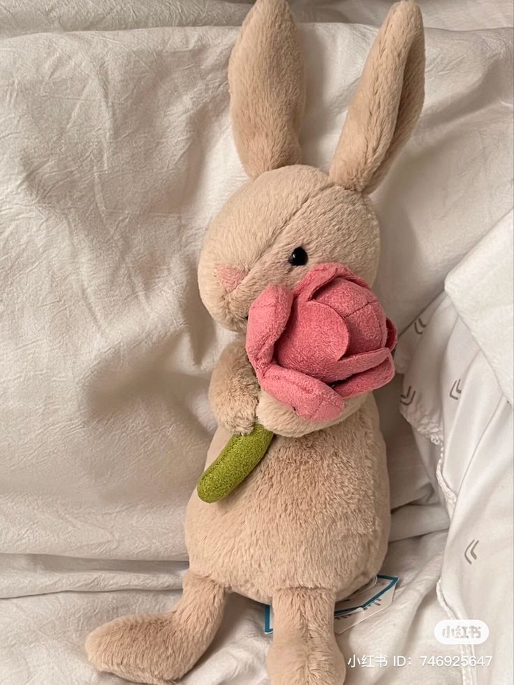 a stuffed rabbit holding a pink rose in its mouth