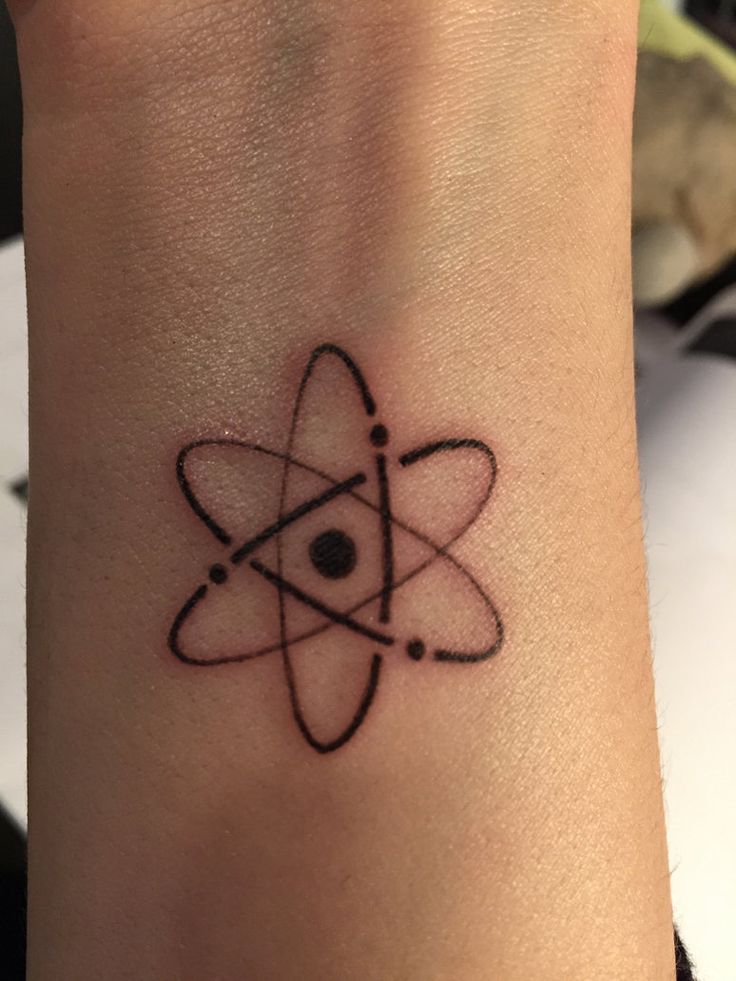 a black and white photo of a wrist tattoo with an atomic symbol on the wrist