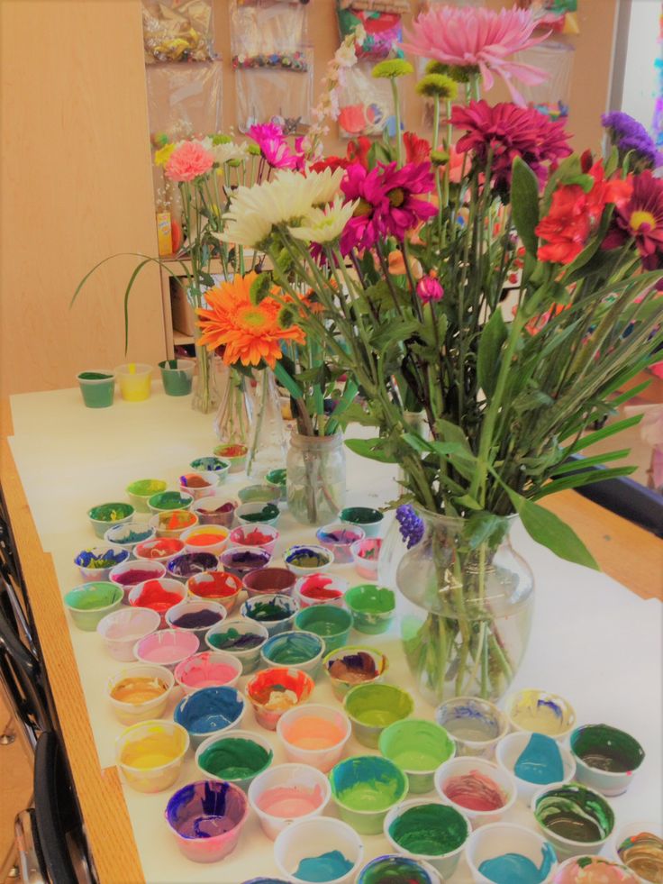 the table is covered with many different colored paints and vases filled with colorful flowers