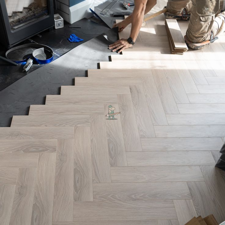 two men working on herringbone flooring in a room with an open fire place