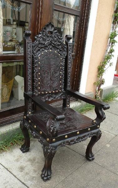 an ornate wooden chair sitting on the sidewalk in front of a storefront with glass windows