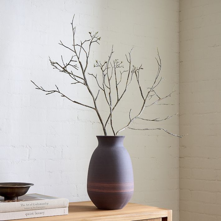 a vase with branches in it sitting on a table next to books and a bowl