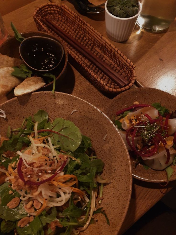 two plates of food on a table with bread, salad and wine in the background