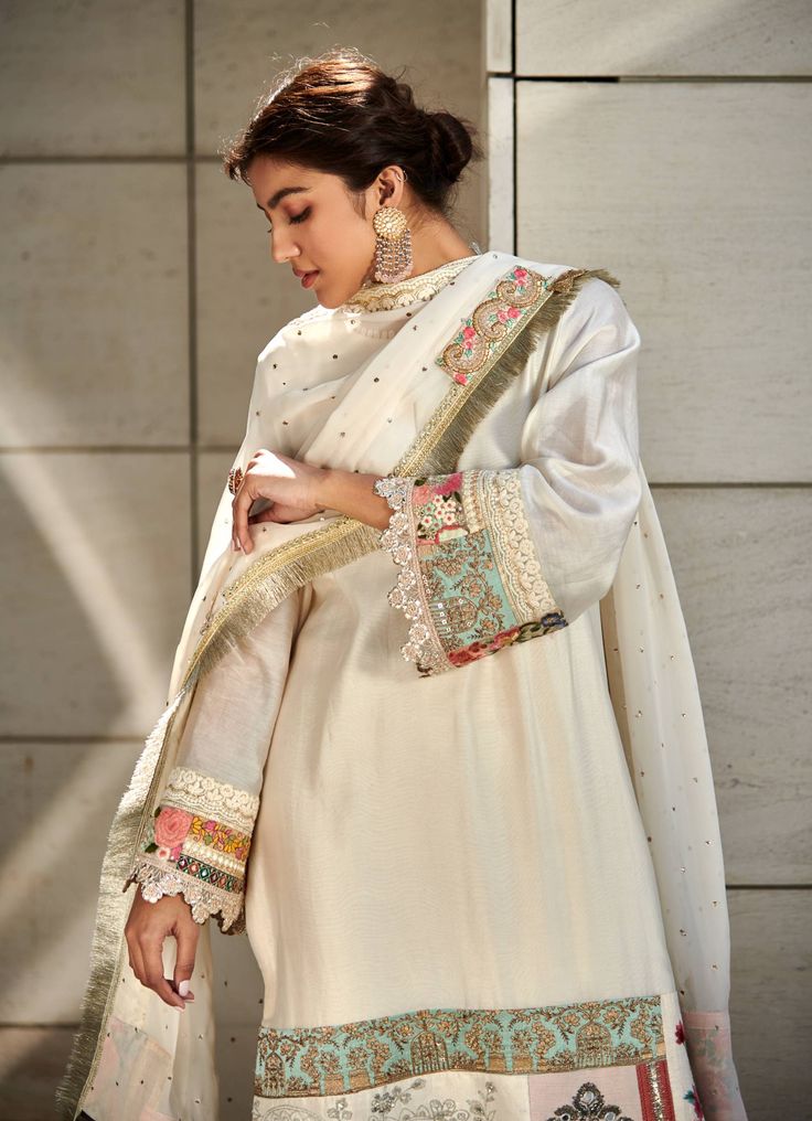 Editor's Note Featuring an ivory chanderi kurta enhanced with patchwork along the hemline. It is paired with ivory chanderi trousers and a georgette dupatta accentuated with mukesh, lace and patchwork border. Fabric: Chanderi: kurta & trousers, dupatta: georgette Color: Ivory Component: Kurta, trousers & dupatta Sleeve type: Full Neckline: Round Occasion: Festive Care: Dry Clean Only About the Designer Varun’s work marries the beauty of heritage Indian handcrafted embroideries with a modern colo Off-white Palazzo Set With Dupatta And Straight Kurta, Cream Cotton Silk Kurta With Traditional Drape, Bollywood Style Chanderi Palazzo Set In Off White, Bollywood Style Off White Chanderi Palazzo Set, Festive Off-white Palazzo Set With Embroidered Border, Unstitched Off White Sharara With Embroidered Border, Transitional Off White Kurta With Dupatta, Transitional Off-white Kurta With Dupatta, Festive Off-white Embroidered Sharara