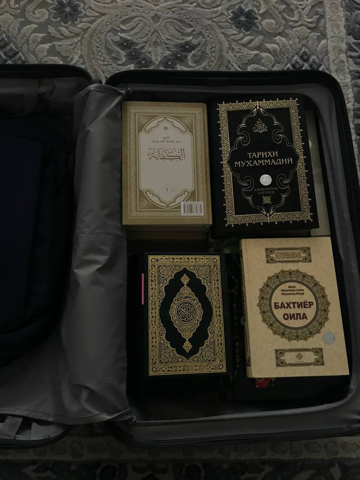 an open suitcase filled with books on top of a carpeted floor next to a wall