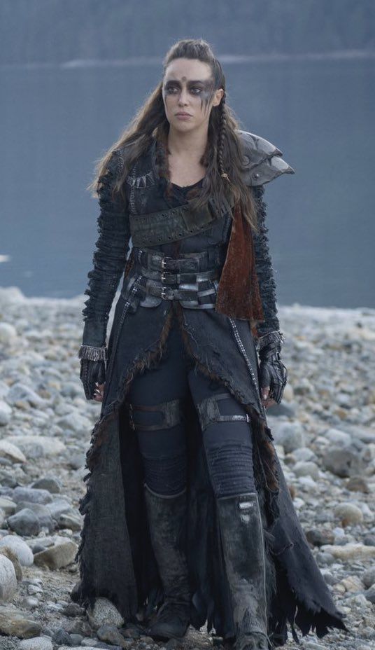 a woman standing on top of a rocky beach next to a body of water with mountains in the background