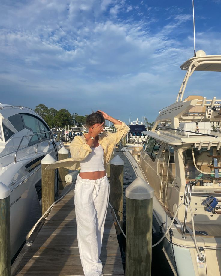 a woman standing on a dock next to a boat in the water with her hands behind her head