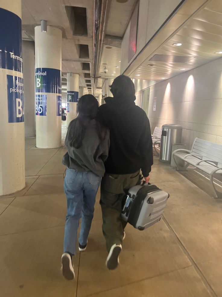 two people are walking through an airport with their suitcases in hand and one is holding the other