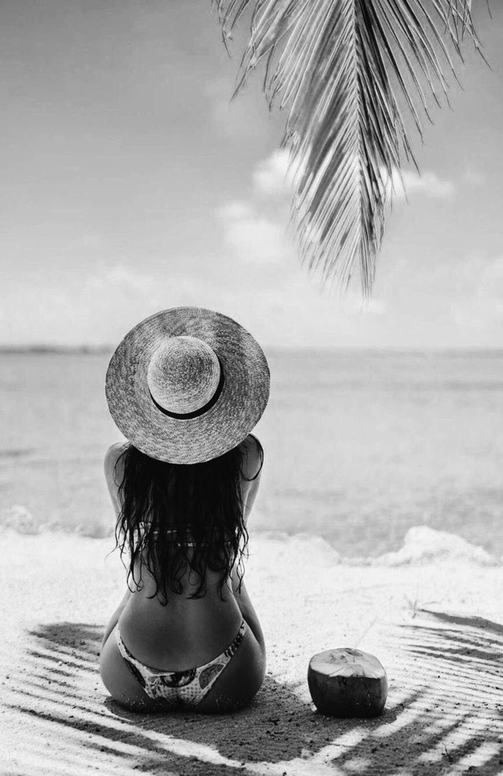 a woman sitting on the beach with her back to the camera, wearing a hat