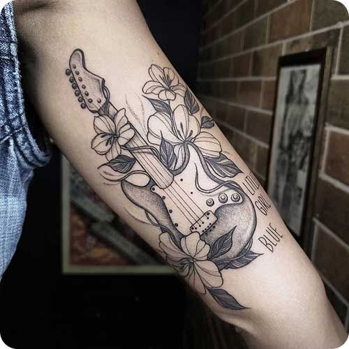 a woman's arm with a guitar and flowers tattoo on the left side of her arm