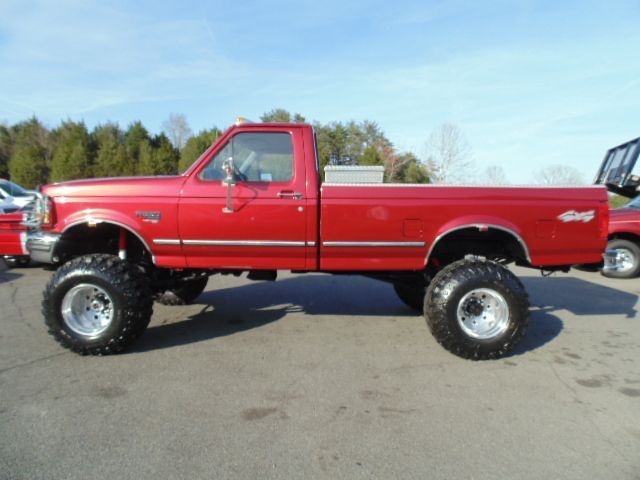 a red truck parked in a parking lot next to other cars and trucks with large tires