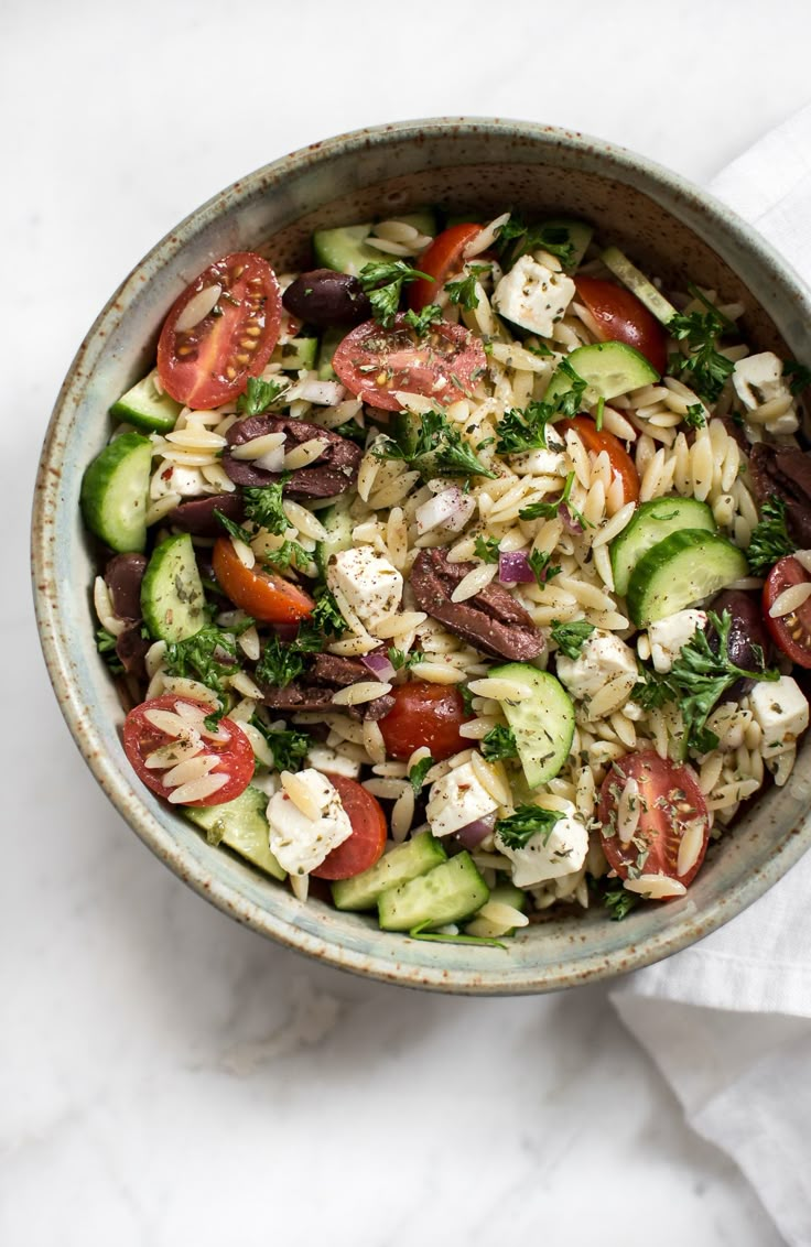 a bowl filled with pasta salad on top of a white countertop next to a napkin