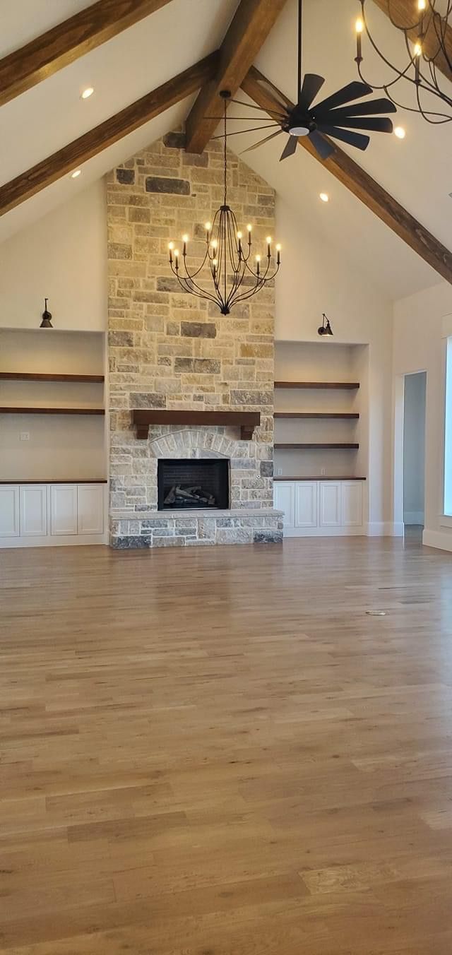 an empty living room with wood flooring and exposed beams on the ceiling is lit by chandeliers