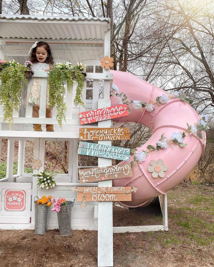 a child's play house with a pink slide and flower potted planters