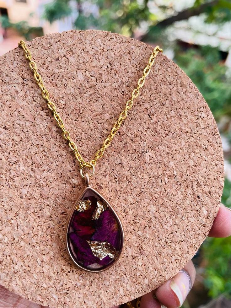 a person holding up a necklace with a purple tear shaped pendant on top of it