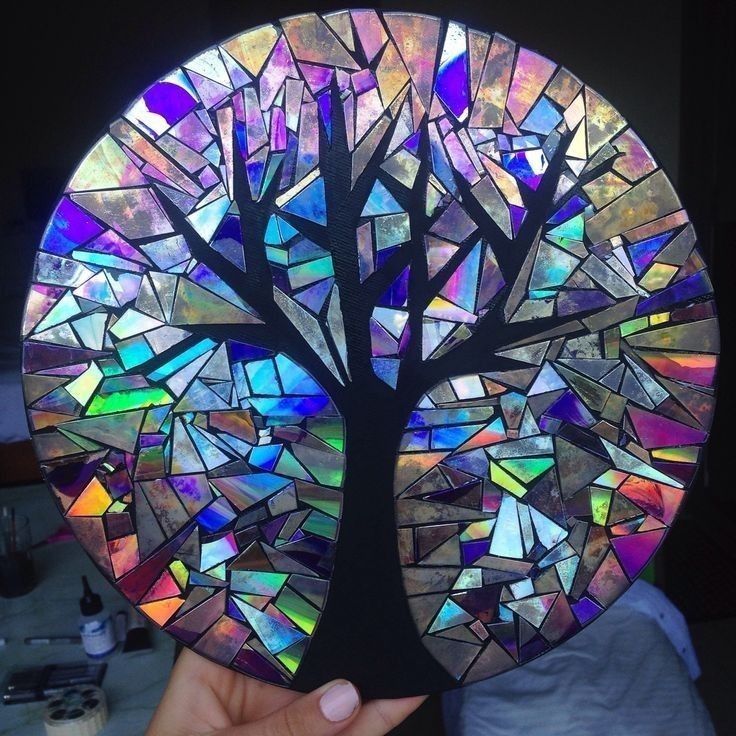 a person holding up a stained glass plate with a tree on it's side