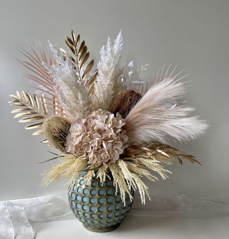 a vase filled with flowers and feathers on top of a white tablecloth covered table