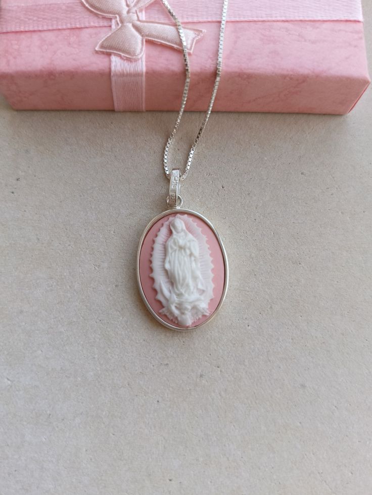 A handmade sterling silver pendant holding a resin pink and white cameo featuring Our Lady of Guadalupe. The back is all covered in solid silver. Measurement of pendant excluding bail is 3.00 cm x 2.00 cm Please note the items are shiner than shown in photos.and colour may vary a bit in photo.  All items will be sent by registered airmail in a jewelry gift box and an organza bag. You can view more of my work in this Etsy shop or Facebook page TrulyFiligree.