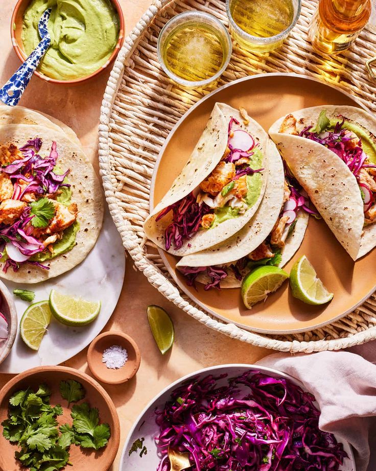 three tacos and two bowls of coleslaw on a table with lime wedges