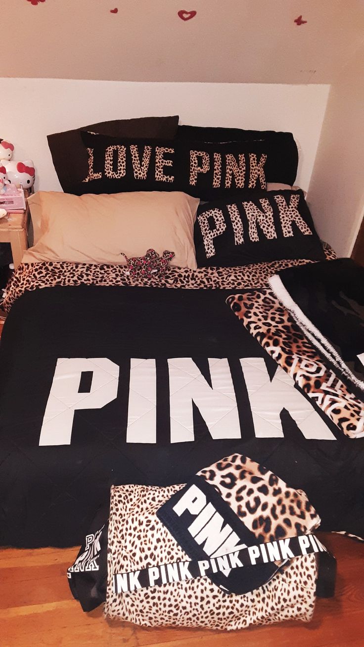 a bed with black and pink pillows on top of it next to a wooden floor