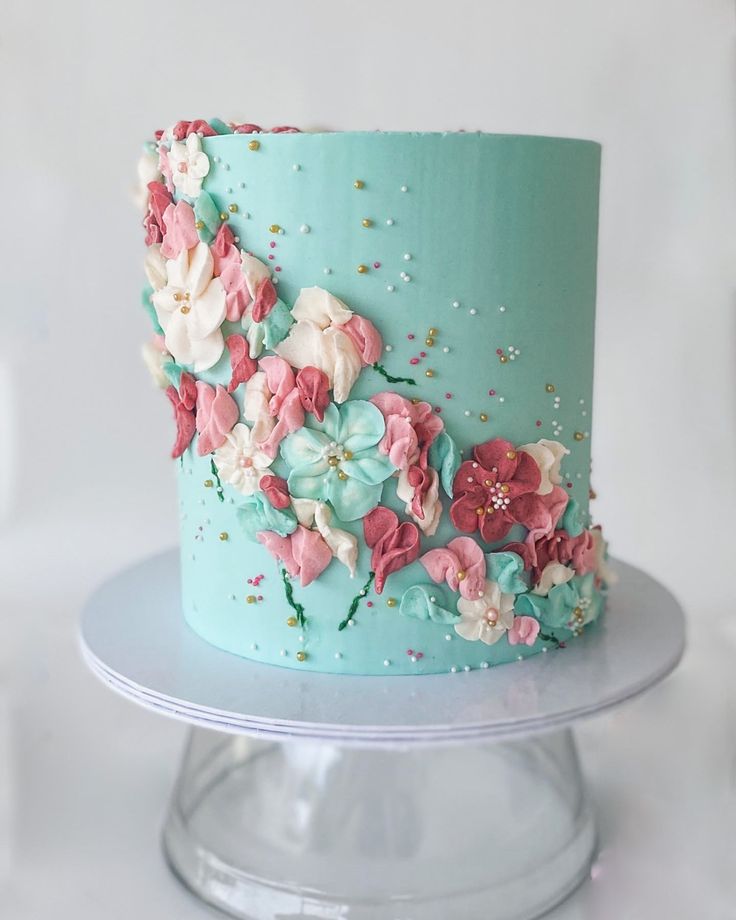 a blue cake with pink and white flowers on it sitting on top of a plate