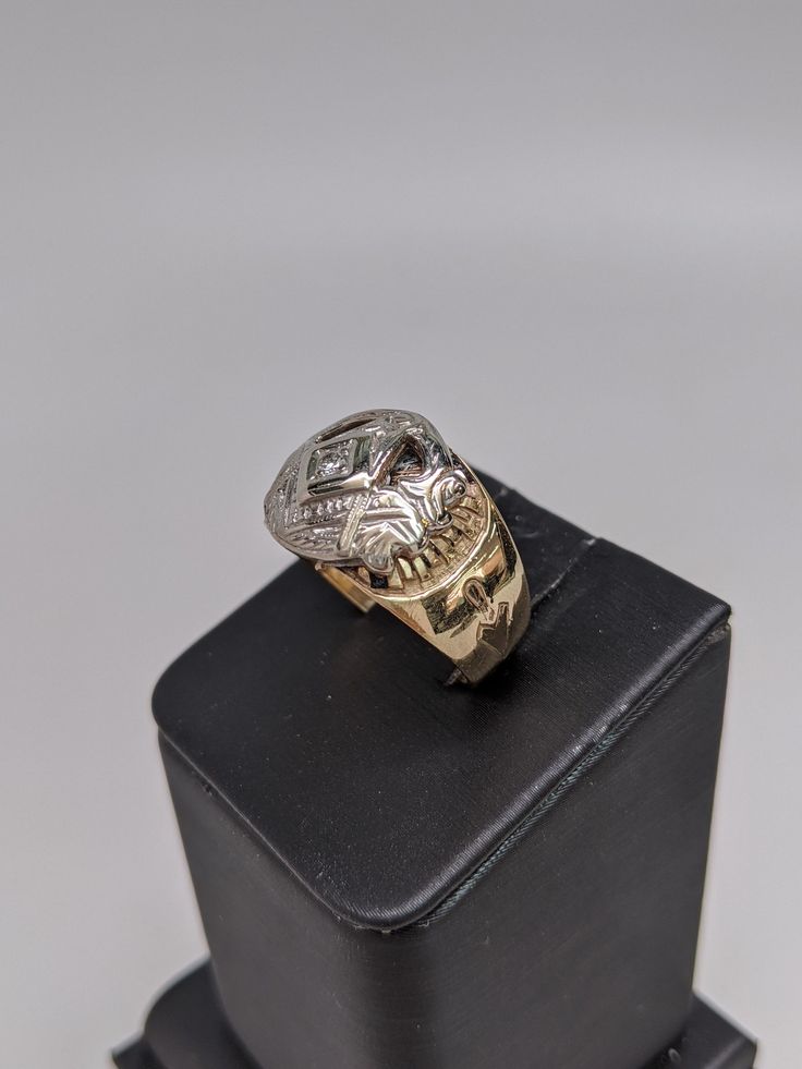 This ring is made of 10k white and yellow gold. The mounting is yellow with different inscriptions made into it. The Masonic symbol is in white gold and has a small round diamond set in the center. The face of the ring is 14mm wide and tapers down. Size 9, but can be resized up or down two sizes free of charge. Symbolic Skull Ring For Anniversary, Symbolic 14k Stamped Engraved Ring, Symbolic Yellow Gold Diamond Ring, Symbolic Yellow Gold Rings With Diamond Accents, Symbolic Engraved Yellow Gold Ring, Hallmarked, Diamond Rings Symbolic For Formal Occasions, Formal Symbolic Diamond Ring, Symbolic Diamond Ring For Formal Occasions, Symbolic 14k Gold Engraved Promise Ring