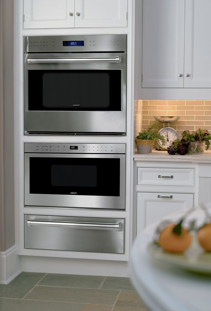 two ovens in a kitchen with white cabinets and counter tops, one is built into the wall