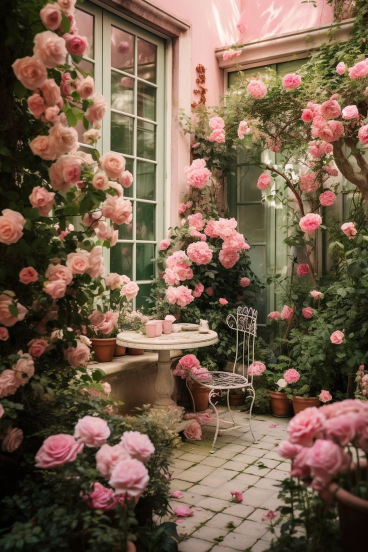 pink roses are blooming in the garden next to a small table and chair with a cup on it