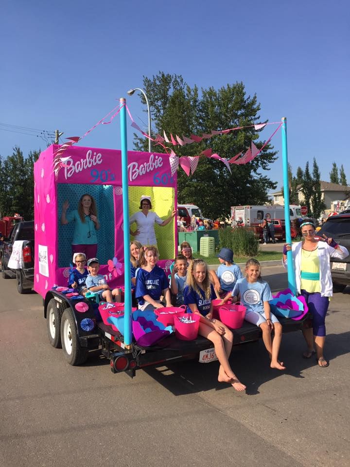 a group of kids sitting on the back of a pink trailer with barbie dolls in it