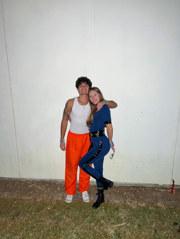 a man and woman standing next to each other in front of a white wall wearing orange pants