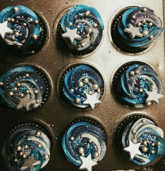 twelve cupcakes with blue frosting and white stars on them in a muffin tin