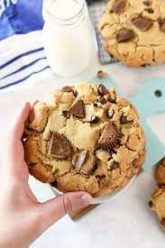 chocolate chip cookies are being held up by someone's hand with milk in the background