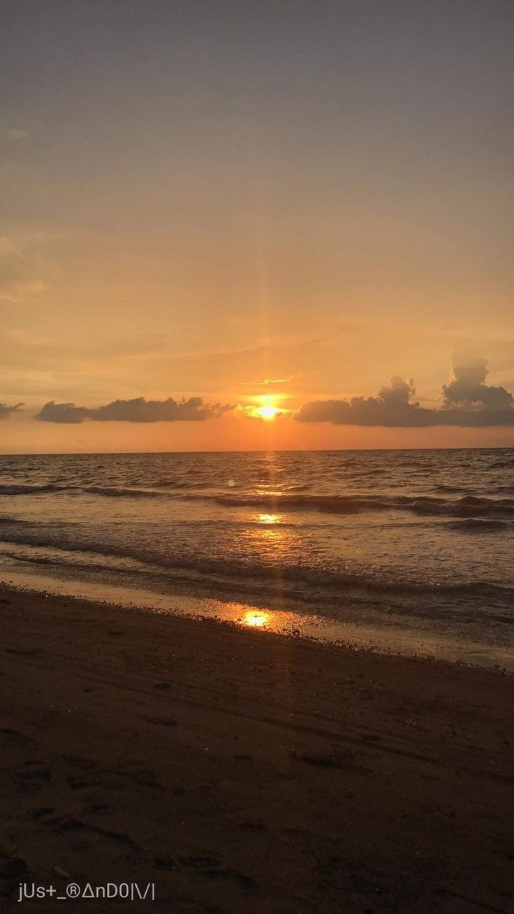 the sun is setting over the water on the beach