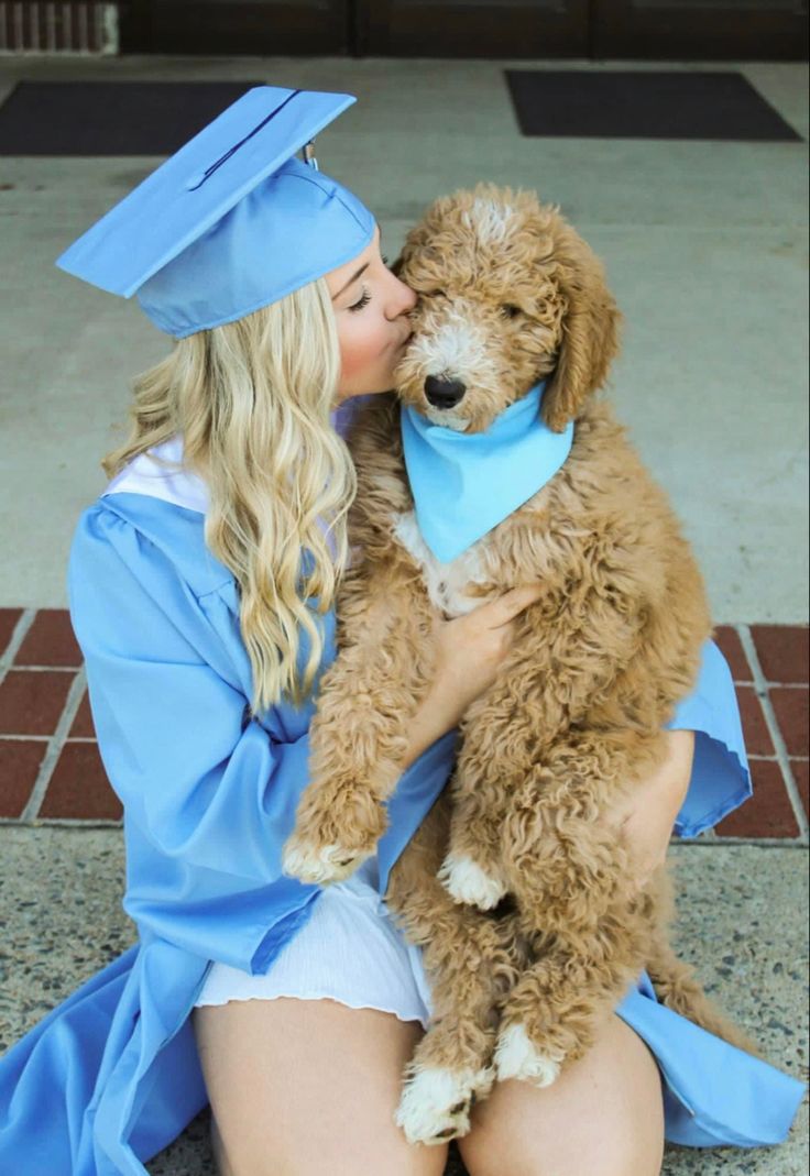 a woman in a graduation cap and gown kissing a dog wearing a blue bandana