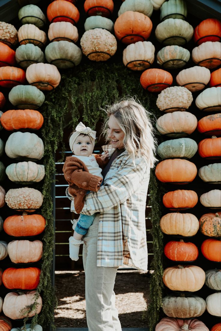 a woman holding a baby in front of a display of pumpkins